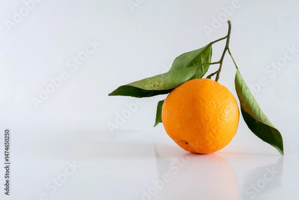 Fototapeta A fresh, rich and healthy orange with leaf resting on white background. Organically grown product