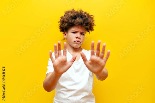 Fototapeta dissatisfied african american boy avoiding refusing and showing palms on yellow isolated background, curly schoolboy teenager showing disgust and stop gesture