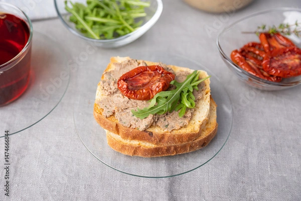 Fototapeta Chicken liver pate with wheat bread, arugula, sun-dried tomatoes and black tea. Homemade traditional rustic cuisine. Breakfast or snack option. Selective focus, close-up.