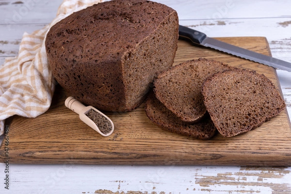 Fototapeta Rye Borodino (Borodinskiy) bread with a crispy crust on a wooden board, cut into slices. Homemade baking in rustic style. Selective focus, close-up.