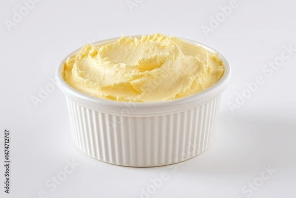 Fototapeta A ramekin of creamy, pale yellow butter sits on a white background.