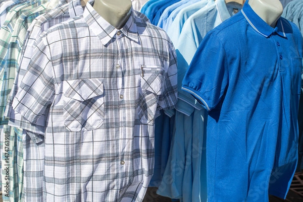 Fototapeta Checkered and blue polo shirts arranged on mannequins in retail store, presenting stylish assortment of summer fashion options for men, perfect for casual and elegant looks,overconsumption crisis