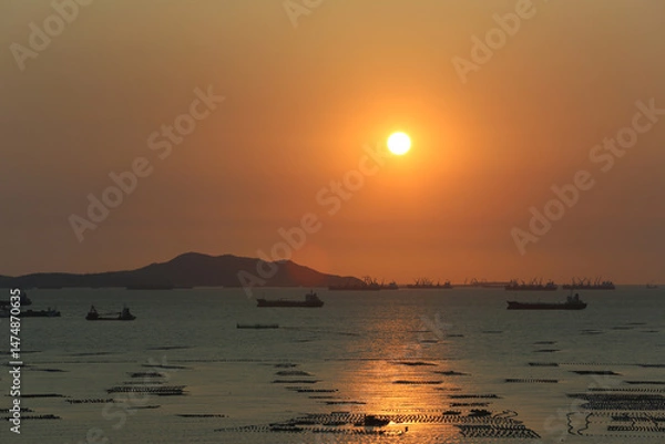 Obraz Sea is filled with cargo ships and fishing boats at dusk.