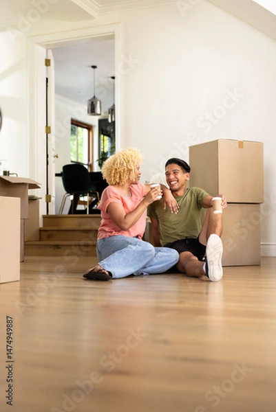 Obraz Young diverse couple sitting on floor enjoying coffee while unpacking in new home