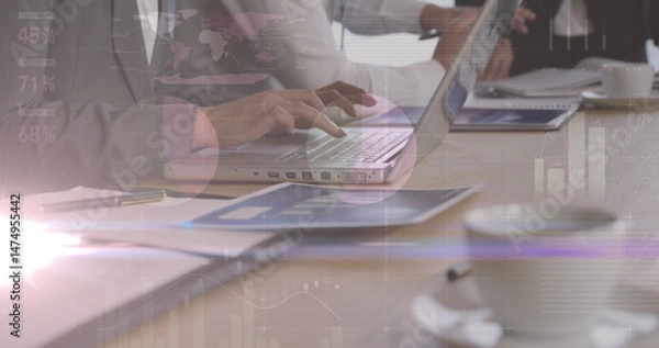 Fototapeta Image of lights and graphs over hands of diverse businesspeople working on laptops