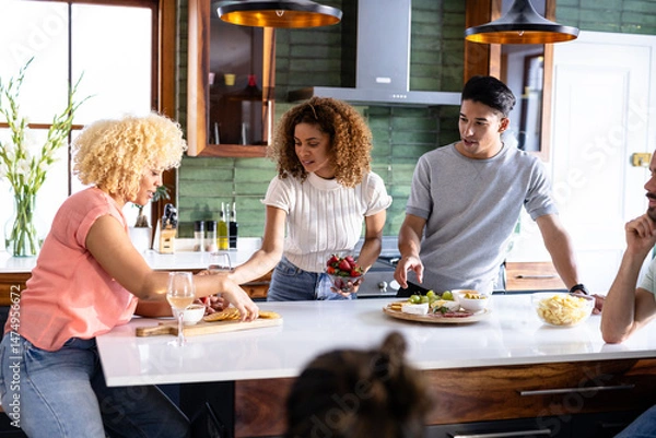 Obraz Diverse friends preparing snacks together in modern kitchen, enjoying casual conversation