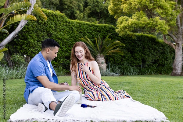 Obraz Young couple enjoying picnic on blanket in park, sharing joyful conversation