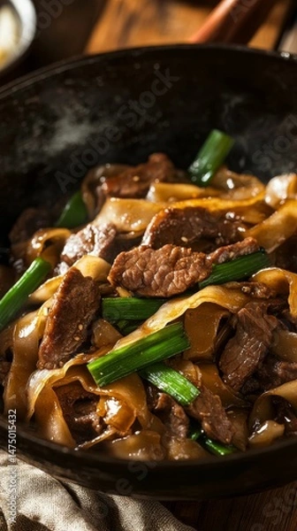 Fototapeta sizzling beef horfun noodles with caramelized onions and scallions close-up view, stir fry beef noodle