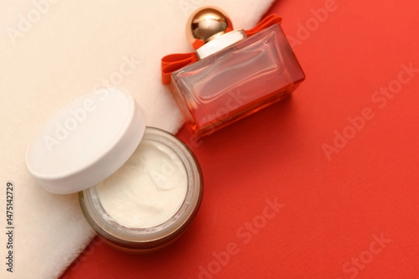 Obraz Cosmetic cream on white towel and perfume container on red background.
