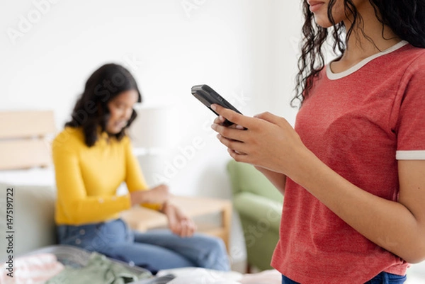 Obraz Teen using smartphone while mother sits on bed, both enjoying relaxed moment