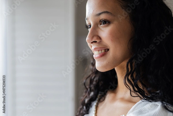 Fototapeta Smiling woman looking out window, feeling hopeful and inspired at home