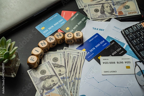 Obraz Business and finance background image showing a blend of paper currency, credit cards, profit charts, tax files, and an office setup. The word “FINANCE” arranged with wooden letter blocks.