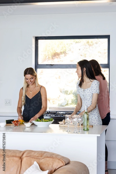 Obraz Preparing salad together in kitchen, friends sharing conversation and laughter