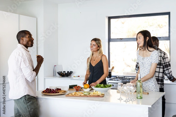 Fototapeta In kitchen, friends preparing food and chatting while gathering around counter