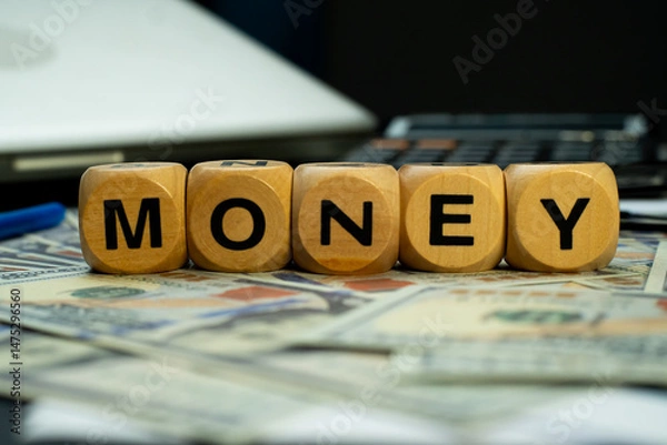Fototapeta wooden block with "MONEY" written on it arranged on top of several dollar bills, with an eye level view. This image is ideal for use in business and financial backgrounds.