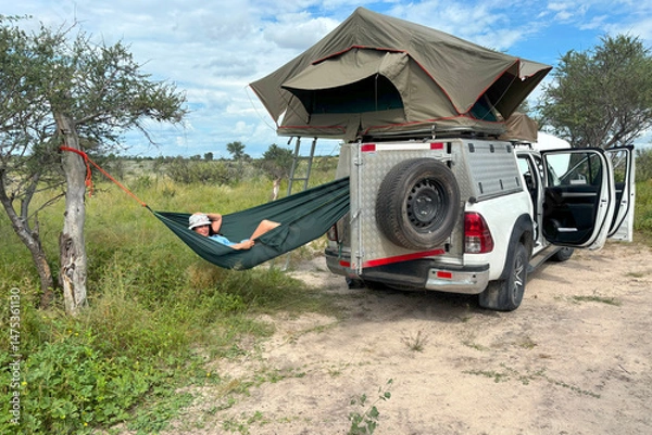 Fototapeta A dark-haired woman in a safari outfit relaxes in a hammock in the African wilderness. Adventure in the Central Kalahari, Botswana. 