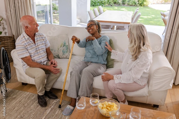 Obraz Senior friends laughing and chatting on sofa, enjoying time together at home