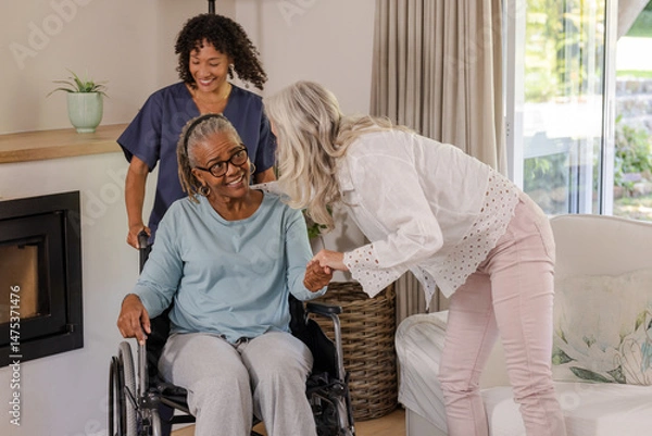 Fototapeta Caregiver assisting senior woman in wheelchair while friend visits at home