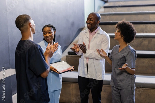 Obraz Celebrating in hospital stairwell, medical team clapping for colleague receiving award