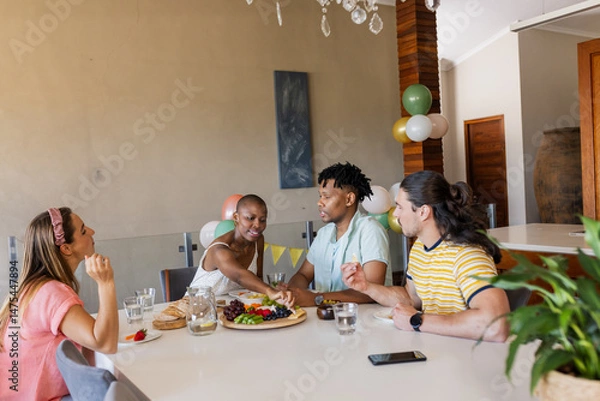 Fototapeta Friends enjoying conversation and sharing snacks at home during casual gathering