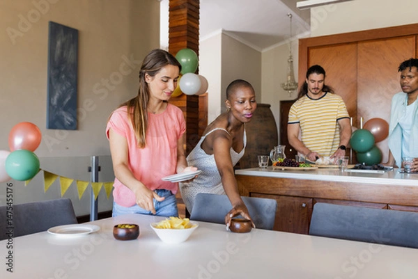 Fototapeta Friends preparing snacks and setting table for indoor gathering at home