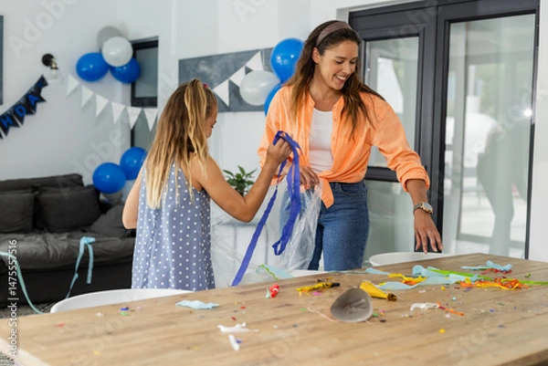 Obraz Mother and daughter cleaning up after birthday party at home, smiling together