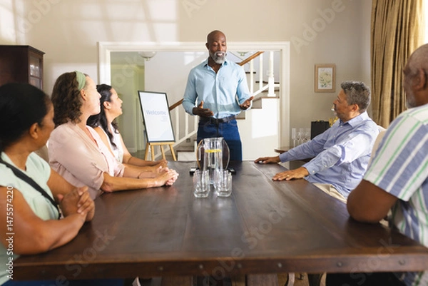 Obraz Senior man leading group discussion at home, engaging with attentive audience