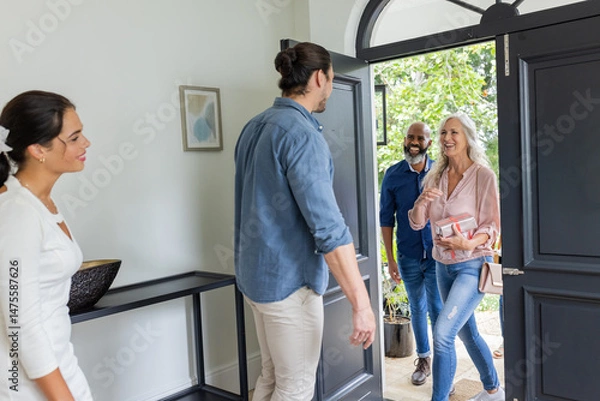 Obraz Welcoming guests at home, smiling couple greeting friends at front door