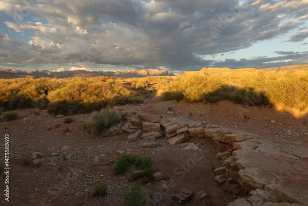 Fototapeta A ledge of broken sandstone in a dry ravine leads the eye in a gently curving line towards the sunlit desert and the distant mountains of Zion NP in Southern UT USA on a spring evening at sunset.