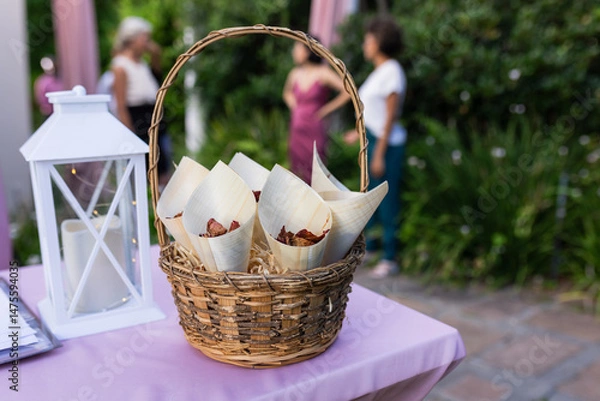 Obraz At outdoor wedding, basket of snacks on table with guests mingling nearby