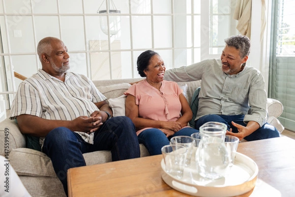 Fototapeta Seniors sitting on couch at home, laughing and enjoying conversation together
