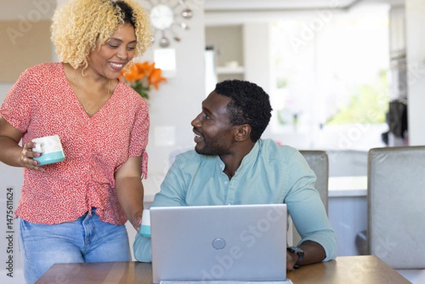 Obraz Smiling friends enjoying coffee while working on laptop at home