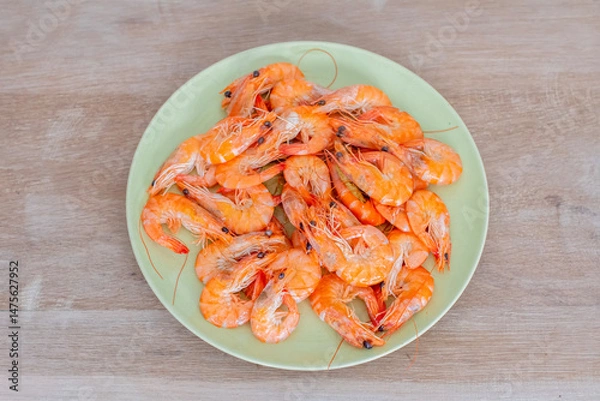 Fototapeta Cooked shrimps arranged neatly on a light green plate, resting on a wooden table, create an inviting and simple seafood presentation that highlights the deliciousness of this meal