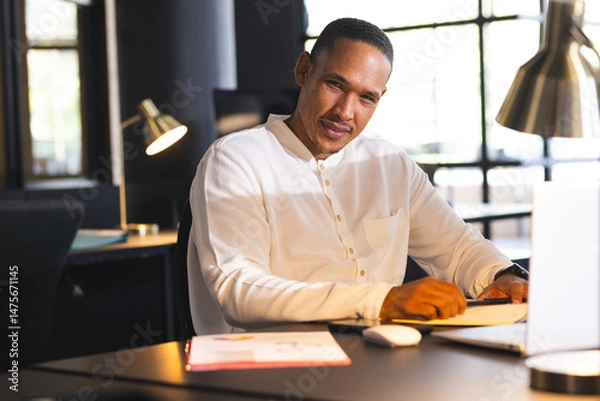 Obraz Businessman in white shirt working late at office, using laptop and smiling