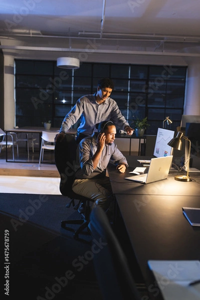 Obraz Businessmen working late in office, discussing project on laptop with focus
