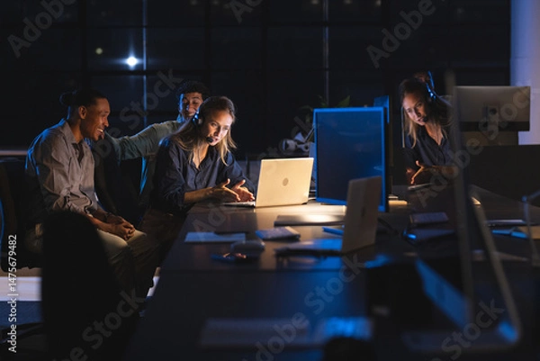 Obraz Team collaborating on project at night in modern office, using laptops and headsets