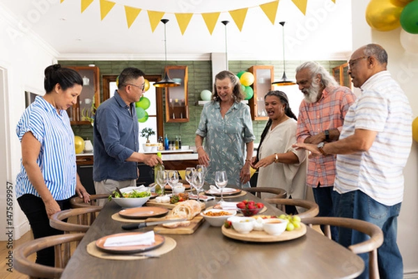 Fototapeta Gathering around dining table, senior friends preparing meal and having conversation