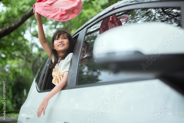 Fototapeta Child enjoys a joyful ride with arms raised through car window in a green park setting on a sunny day