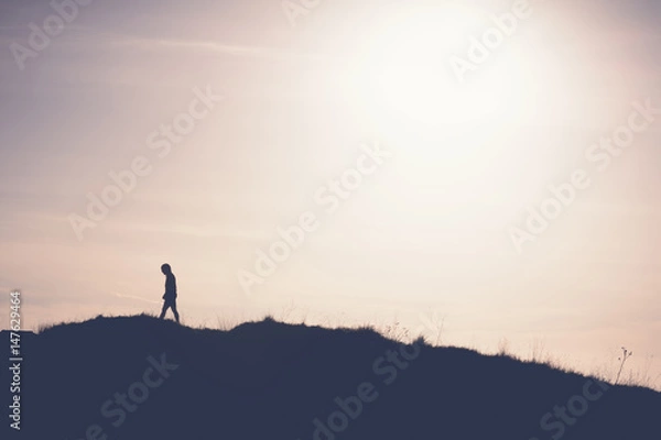 Fototapeta Man walking away from the sun on the hill. Artistic silhouette retro washout edit.