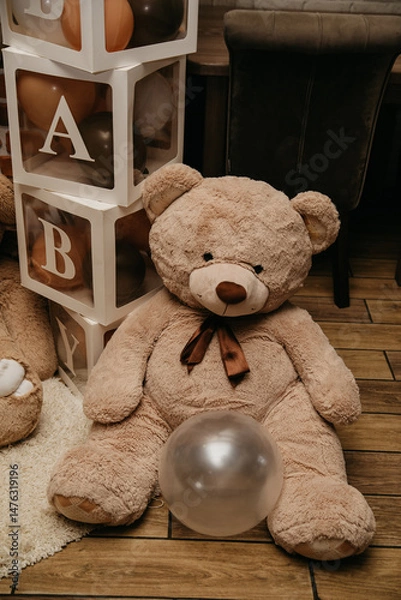 Obraz A brown teddy bear with a brown collar around its neck is near the photo zone on the day of the celebration of the year since the birth of the child with an inflated silver balloon between its paws