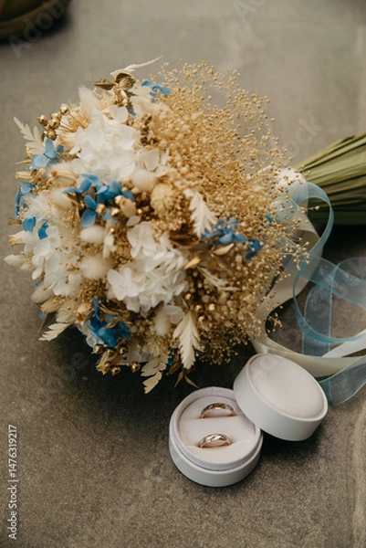 Obraz A bouquet of flowers for a wedding or wedding anniversary celebration wrapped in a decorative ribbon lies next to a box for a pair of gold wedding rings