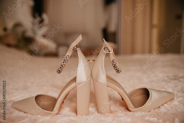 Obraz A pair of beige women's shoes with a gemstone buckle facing away from each other and holding a gold wedding ring in a hotel room on a wedding day or anniversary celebration for a bride