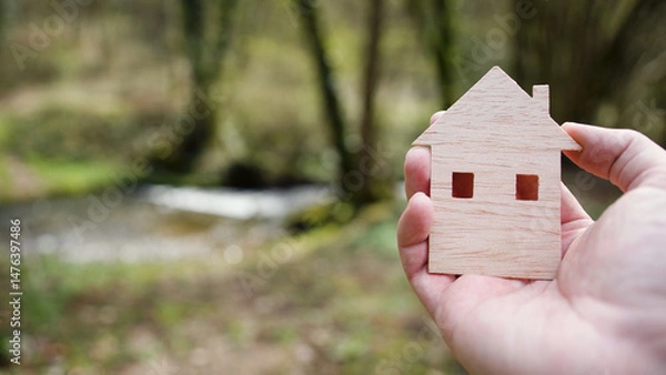 Obraz A man's hand holds a wooden model of a house in the air with a natural background.