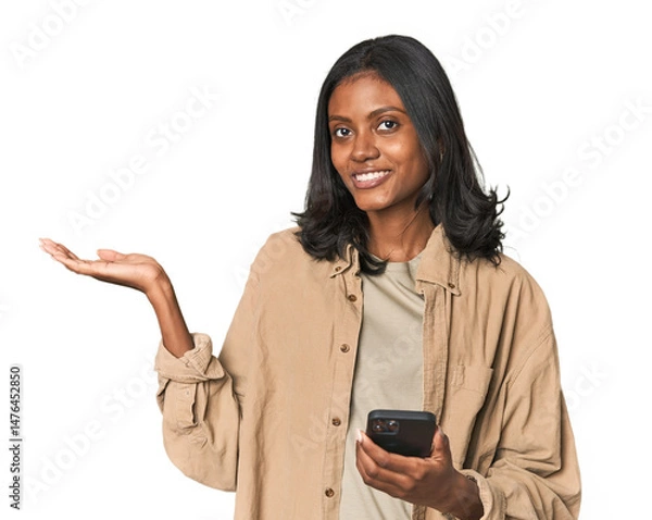 Fototapeta Young Indian woman using a smartphone showing a copy space on a palm and holding another hand on waist.