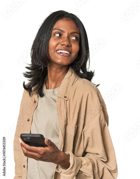 Fototapeta Young Indian woman using a smartphone looks aside smiling, cheerful and pleasant.