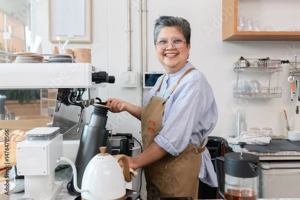 Fototapeta Senior entrepreneur cafe owner barista chats with female customer at counter, Asian male in apron smiling while presenting croissant plate, espresso machine and shelving frame cozy evening scene