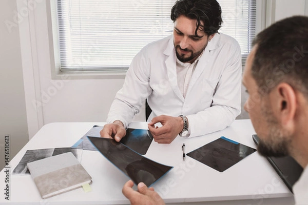 Fototapeta Doctor surgeon traumatologist looks at an X-ray with male petient. fracture, arthrosis, arthritis, joint deformation, dysplasia, meniscus injury. orthopedist specialist consultation