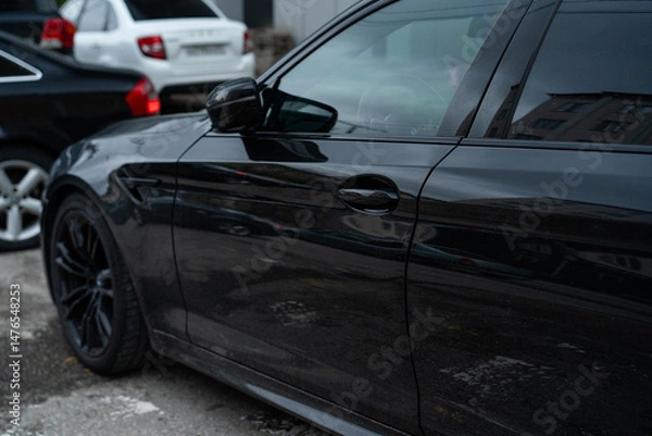 Fototapeta Black luxury car parked among other vehicles in an urban area, showcasing a sleek design and detailed features