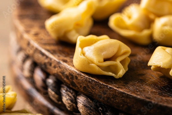 Fototapeta Close up with freshly made tortellini Cappelletti pasta with prosciutto, elegantly arranged on a rustic wooden board with copy space