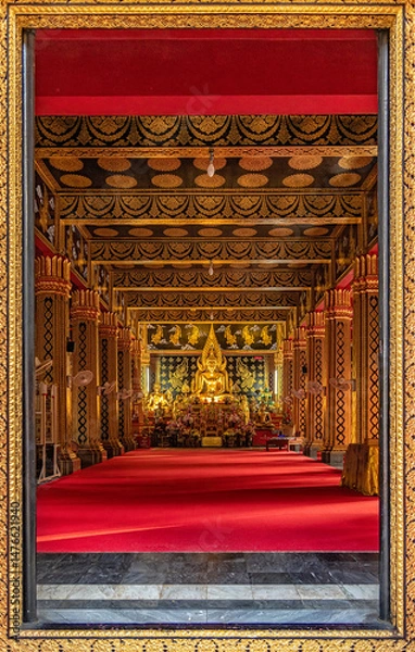 Fototapeta A view through the beautifully carved golden temple door frame shows a large Buddha statue inside a beautifully decorated chapel at Wat Phan On Temple, a popular landmark for tourists in Chiang Mai